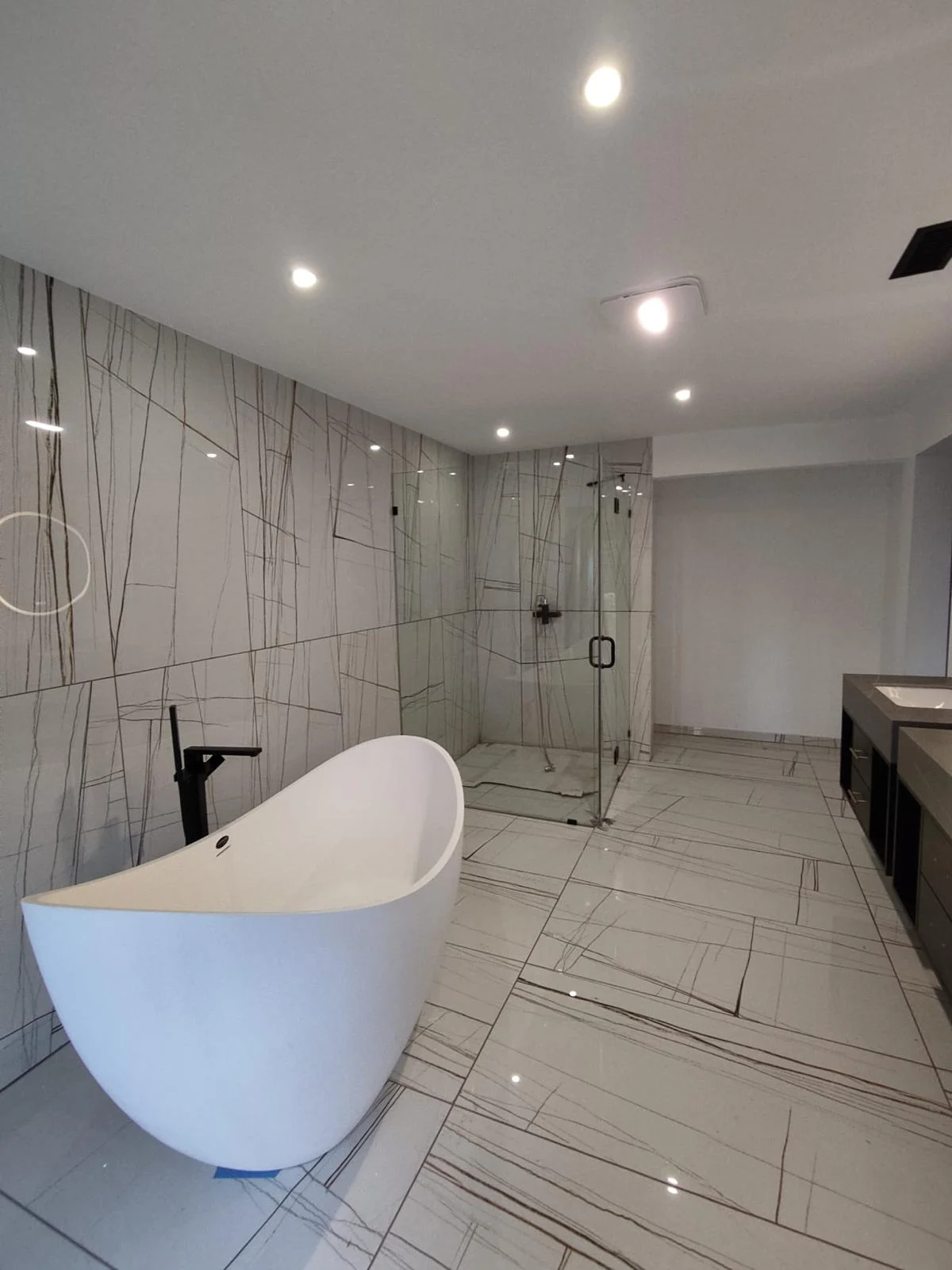 Modern primary bathroom remodel in Bellevue WA featuring a freestanding soaking tub, matte black fixtures, and custom marble-pattern porcelain tile walk-in shower