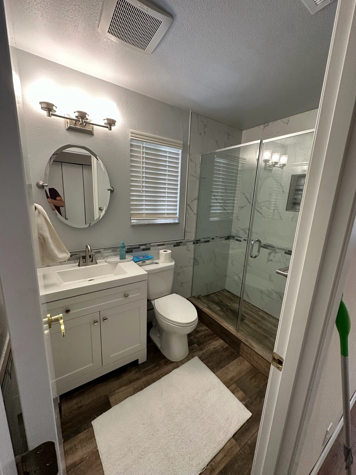 Full bathroom remodel in Bothell WA featuring white shaker vanity, marble-pattern walk-in shower with sliding glass doors, and wood-look tile flooring