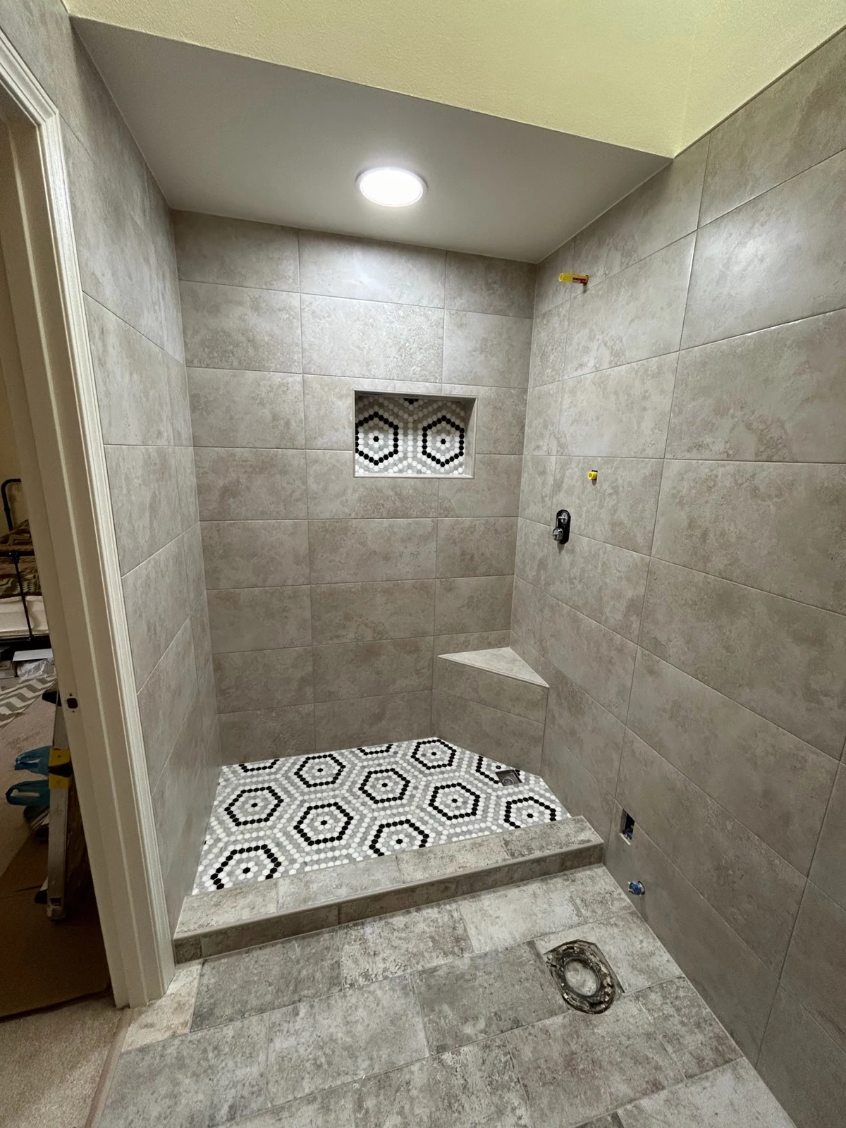 Custom walk-in shower remodel in Issaquah WA featuring stone-look wall tile, geometric hexagon mosaic floor pan, built-in corner bench, and recessed niche