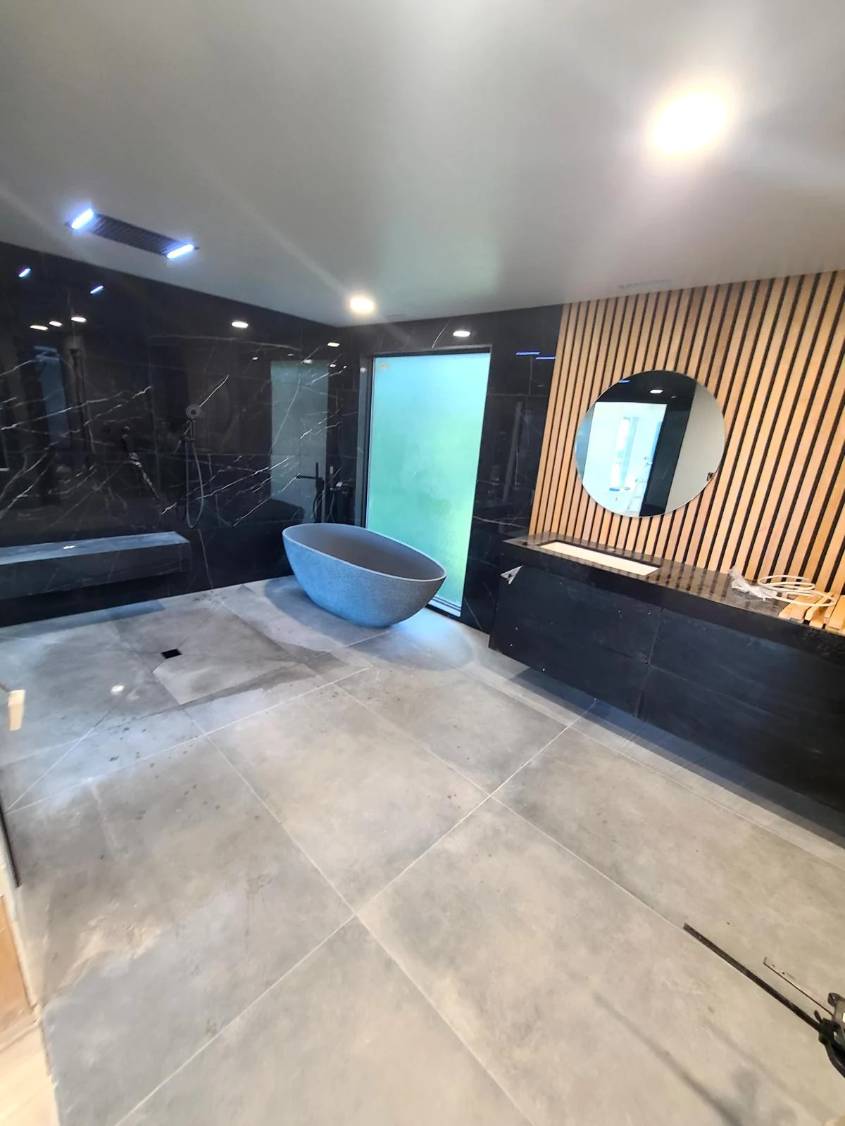 Modern organic spa bathroom remodel in Kirkland WA featuring wood slat accent wall, stone resin soaking tub, black marble wet room, and floating quartz vanity