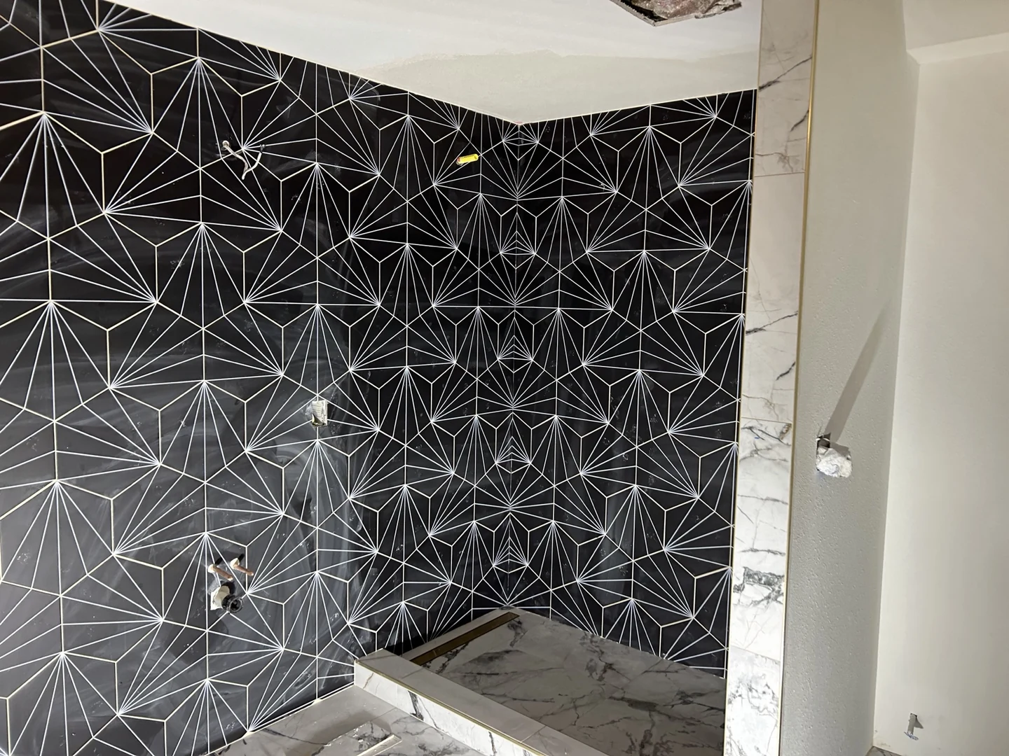 Custom walk-in shower remodel in Sammamish WA featuring black geometric starburst accent tile, marble threshold, and brushed brass linear drain