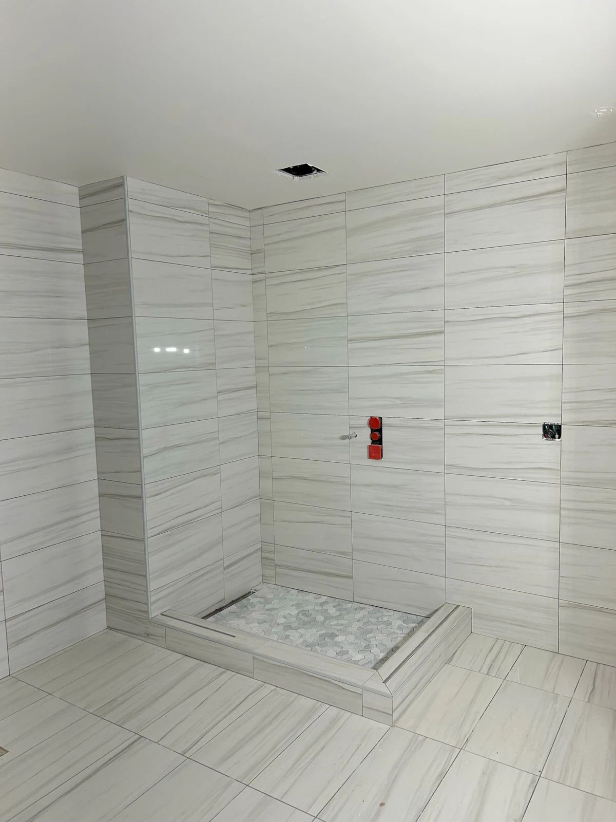 Custom walk-in shower remodel in Woodinville WA featuring linear vein-cut stone tile walls, Carrara marble hexagon mosaic pan, and linear drain